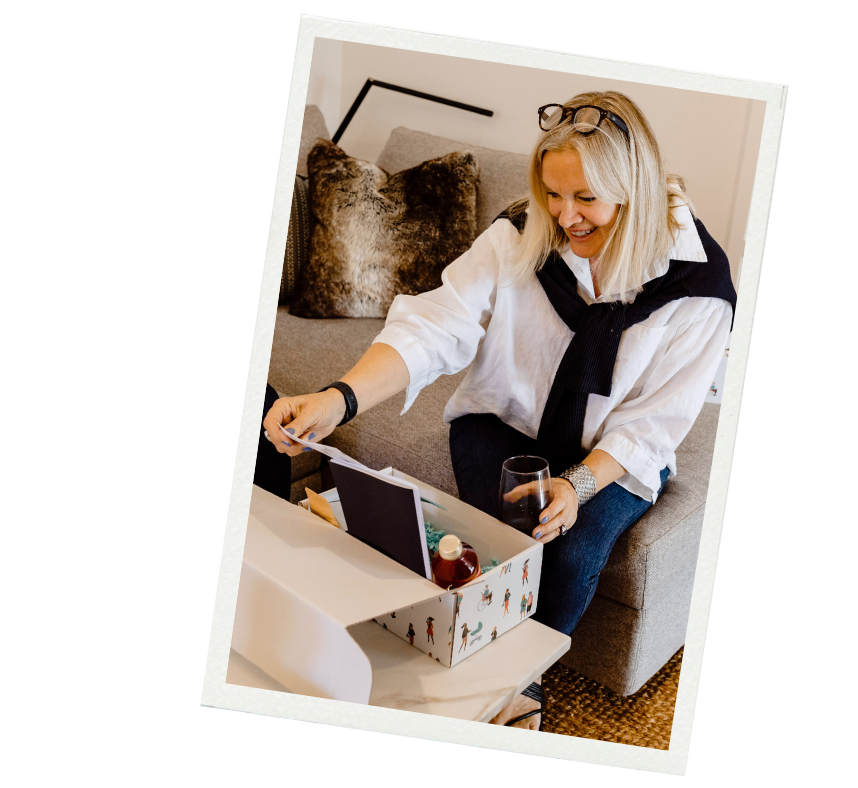 A stylish woman with straight platinum hair leaning over a Zest Self Care Box and looking at the contents with a delighted expression.